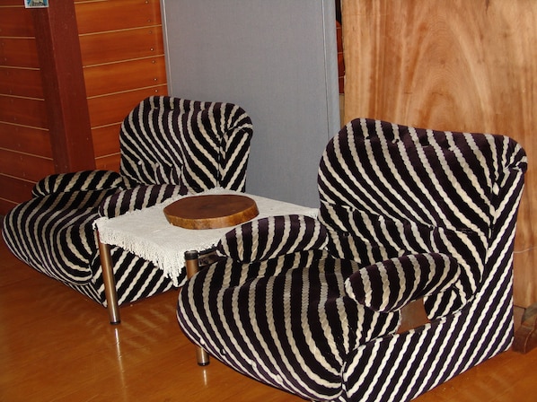 Une pièce avec deux fauteuils à rayures et une petite table en bois recouverte d’une nappe en dentelle blanche.