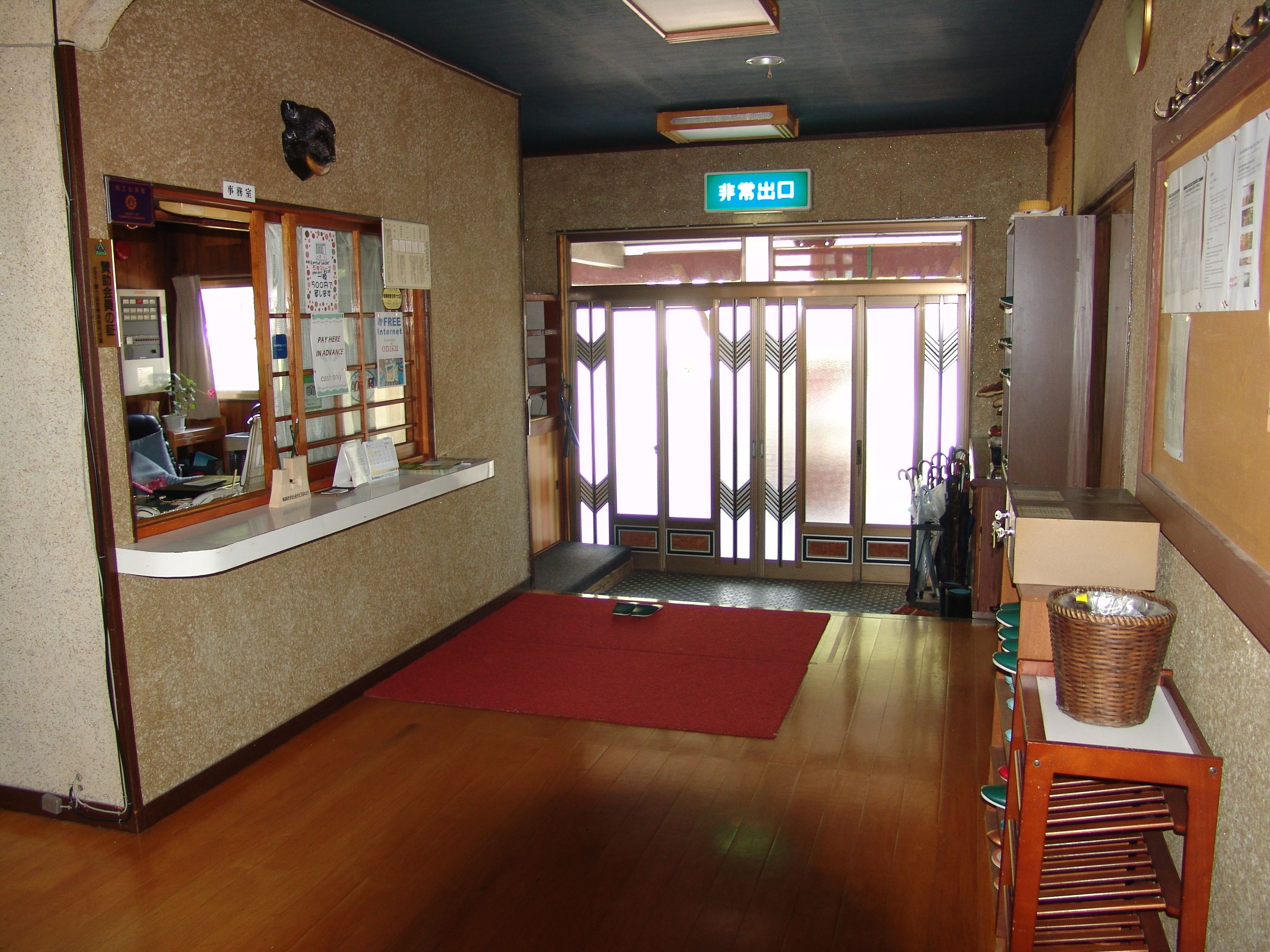 Zona de recepción con mostrador de madera, alfombra roja y señalización de salida.