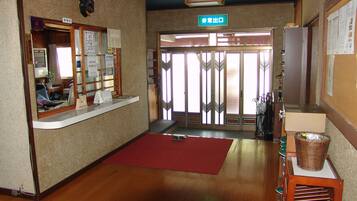 Zona de recepción con mostrador de madera, alfombra roja y señalización de salida.