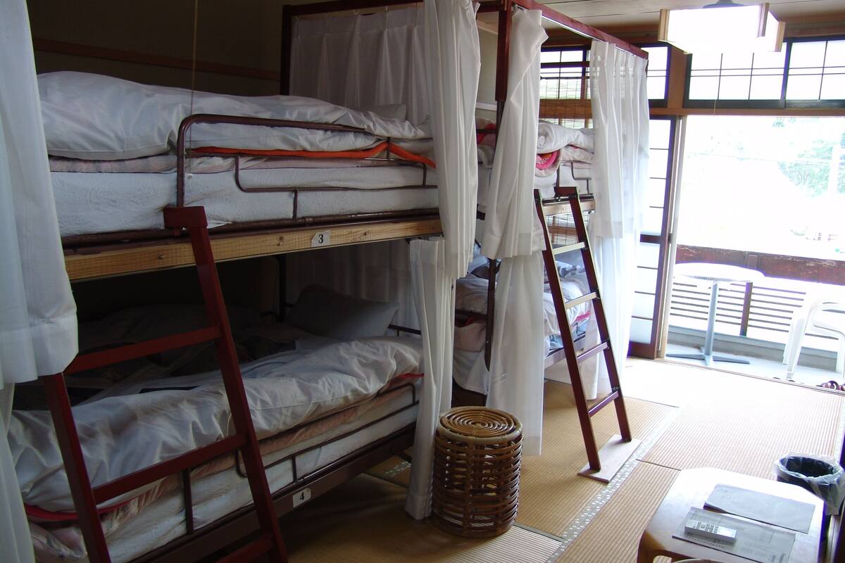 Habitación tipo dormitorio con literas, una escalera, una cesta tejida, una mesita con un control remoto y vistas al exterior a través de una ventana.