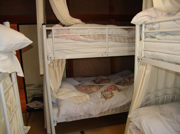 A bunk bed room with white bedding and a floral comforter on the lower bunk. - Towadako Backpackers (Towada)