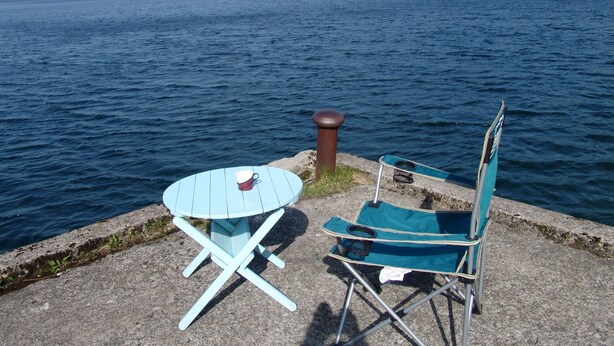 A lakeside setting with a small table and a chair, a metal bollard, and a distant mountain range. - Towadako Backpackers (Towada)