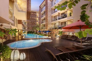 Ein Hotelpoolbereich mit mehreren Pools, Liegestühlen und Sonnenschirmen.