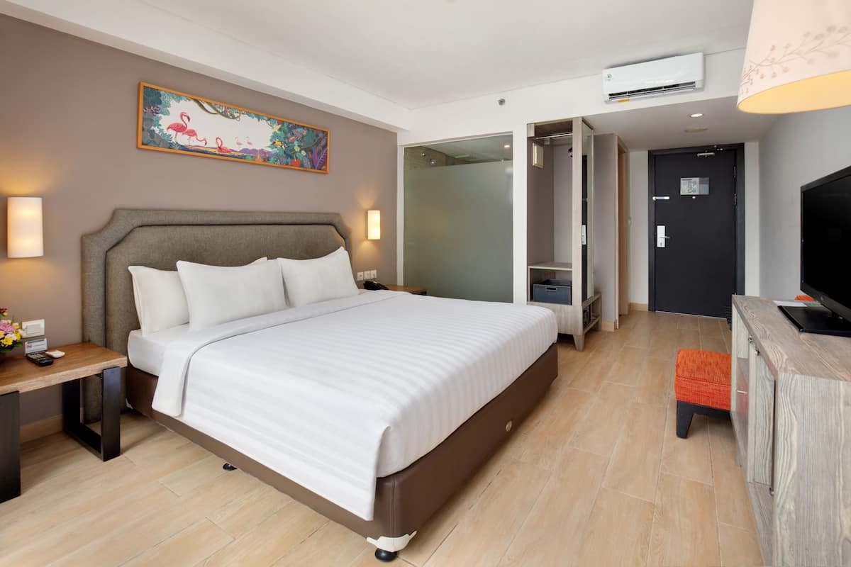 A hotel room with a large bed, bedside tables, a desk, a TV, and a bathroom with a glass shower enclosure.