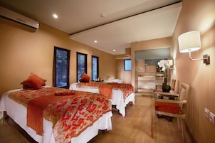 A hotel room with two beds, a sitting area with a chair, a small table, and a mirror.