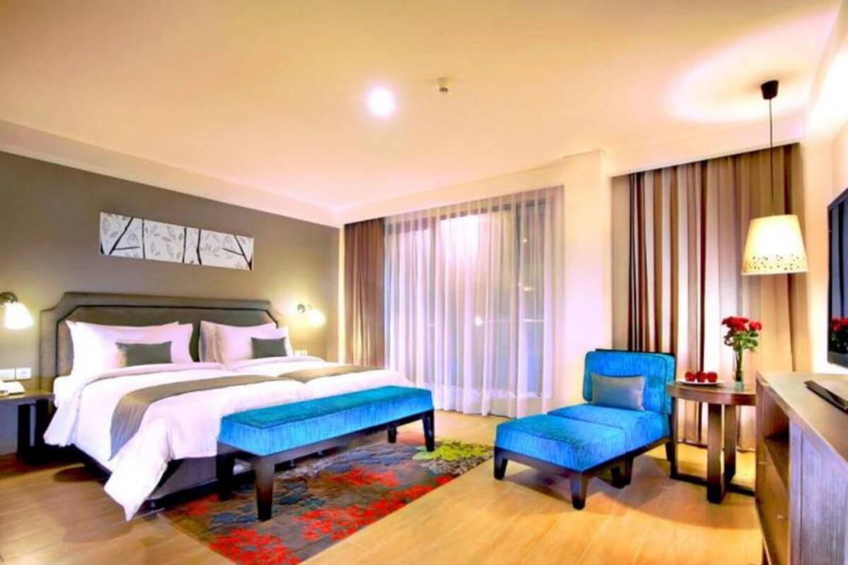 A hotel room with a bed, a desk, a chair, and a large window with curtains.