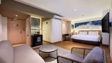 A hotel room with a bed, a sofa, a small table, a TV, and a fireplace.