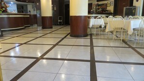 Eine geräumige Lobby mit Fliesenboden, weißen Tischen und Stühlen sowie einem Empfangsbereich mit einer Statue.