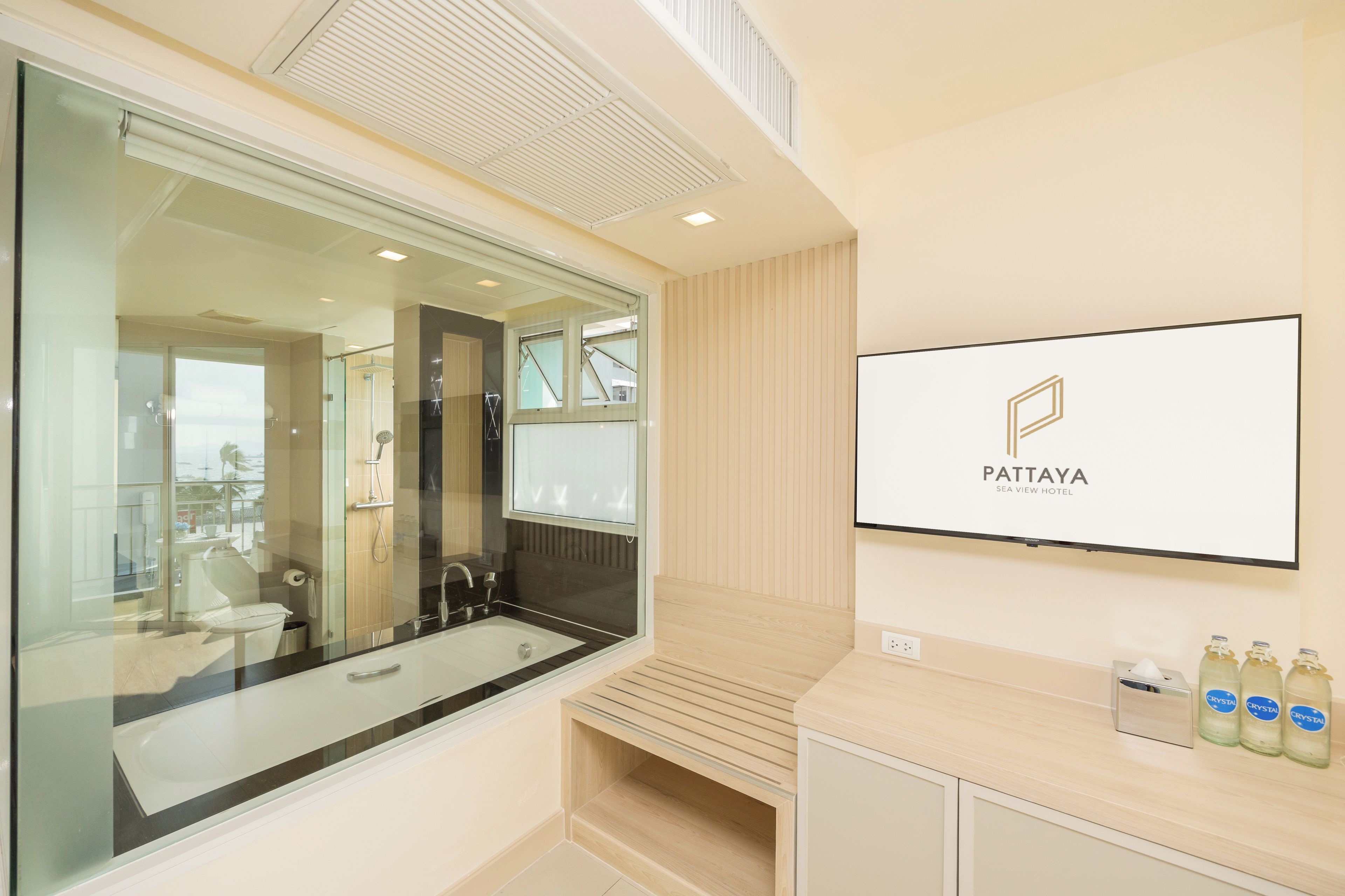 A modern bathroom with a glass-enclosed shower, a vanity with a mirror, and a mounted television displaying the Pattaya Sea View Hotel logo.