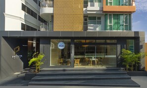 A modern hotel with a glass facade, outdoor seating area, and a visible restaurant inside. - Pattaya Sea View Hotel (Pattaya)