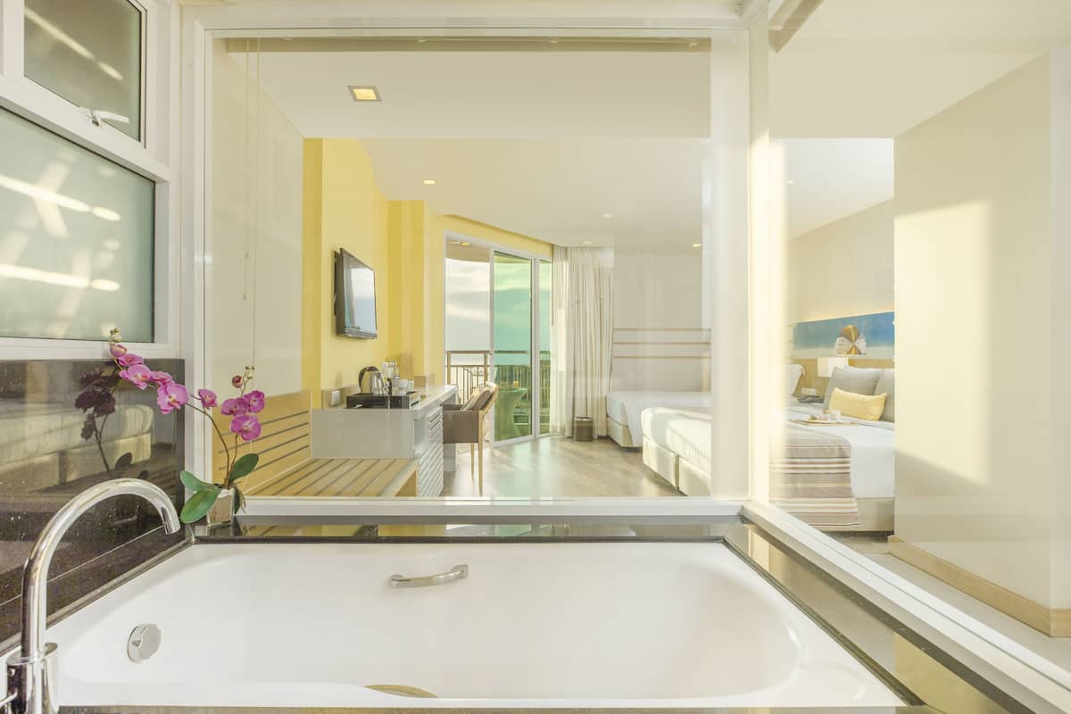 Un baño moderno con una bañera grande, un lavamanos y un espejo. Se ve una ventana con vistas a la habitación.