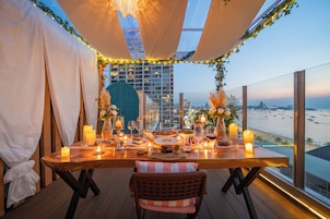 Una mesa lista para cenar con velas, vista a la playa y un paisaje urbano al fondo.