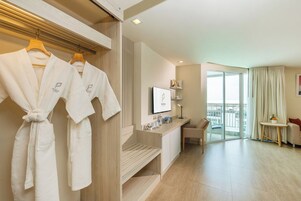 Habitación de hotel con cama, televisor, escritorio y balcón con vistas.