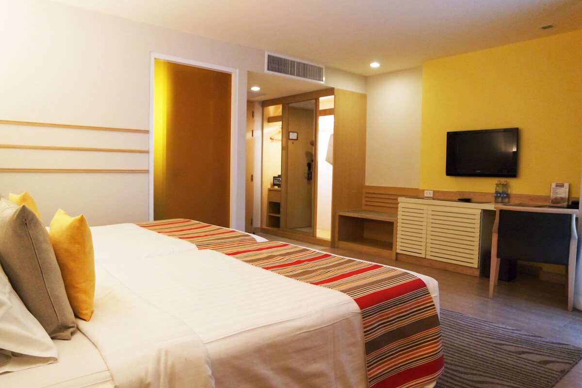 A hotel room with a bed, a desk, a television, and a bathroom visible through an open door.