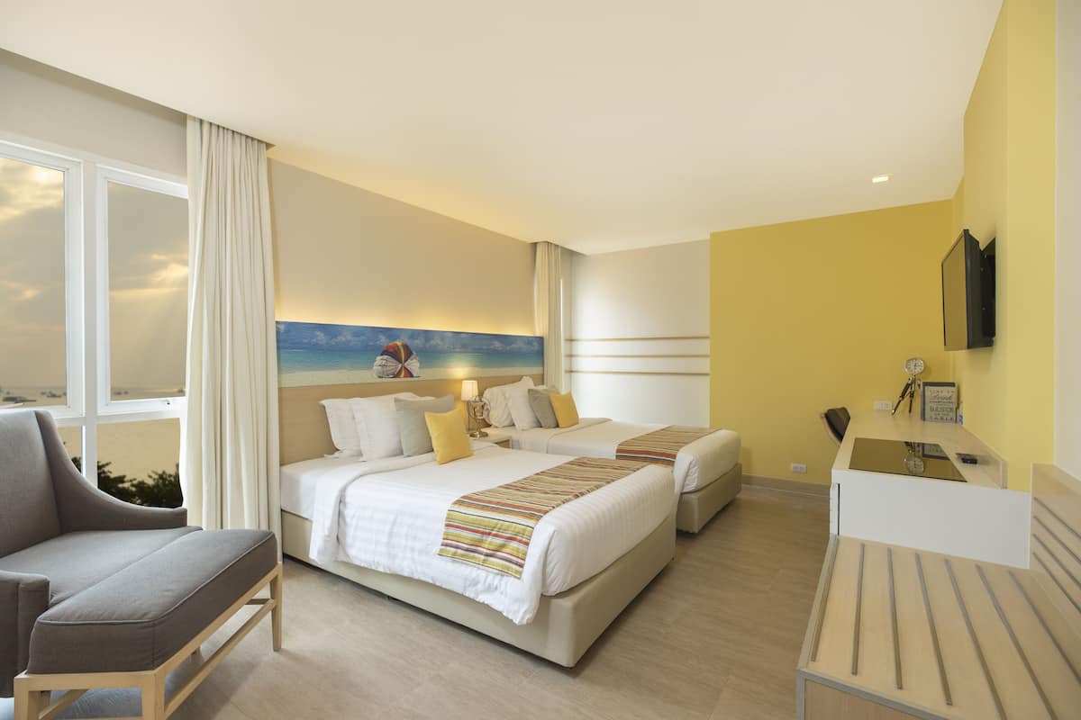 Habitación de hotel con dos camas, un escritorio, una silla y un amplio ventanal con cortinas.