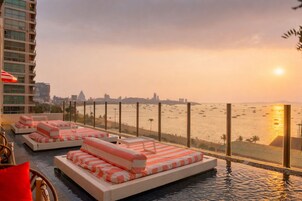Un área de piscina en la azotea con camas lounge y vistas a la playa y el horizonte de la ciudad.