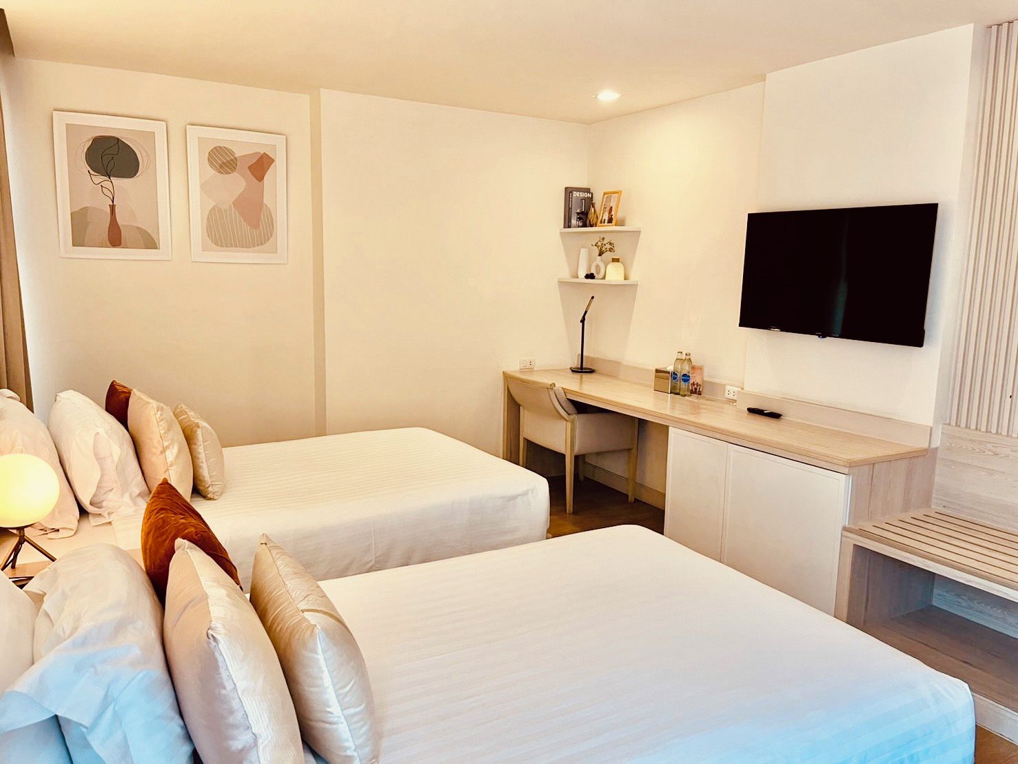 A hotel room with two beds, a desk, a chair, a TV, and artwork on the wall.