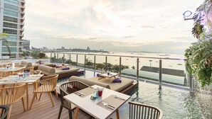 A rooftop bar with outdoor seating, a pool, and a view of the city and beach. - Pattaya Sea View Hotel (Pattaya)