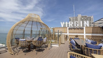 A deck with wicker furniture and a glass dome structure, overlooking the sea.