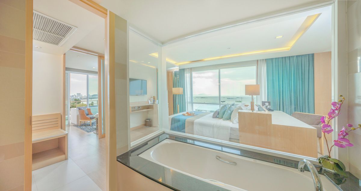 Una habitación de hotel moderna con una bañera grande, una cama con vistas, un escritorio y un área de descanso también con vistas.