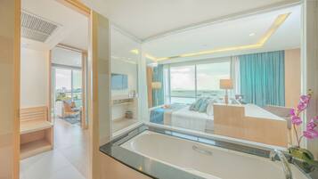 Una habitación de hotel moderna con una bañera grande, una cama con vistas, un escritorio y un área de descanso también con vistas.