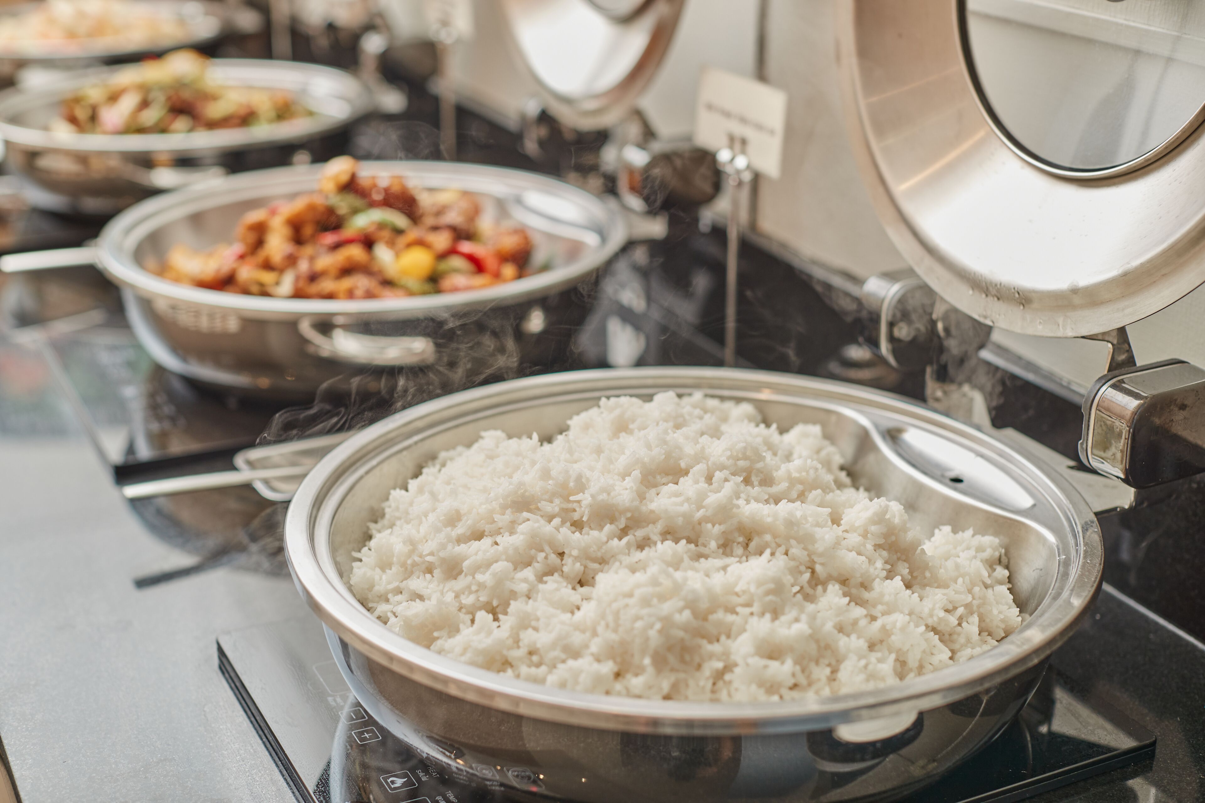 A buffet with various dishes including white rice, stir-fried vegetables, and a dish with chicken and vegetables.