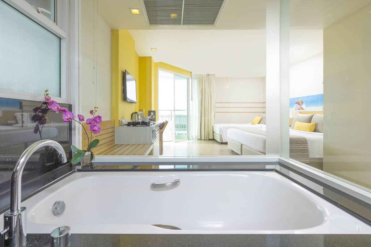 Una habitación de hotel moderna con una bañera blanca grande, un balcón con vistas y una pared de acento amarillo brillante.