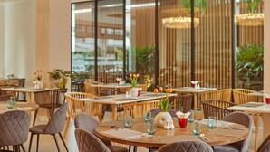 A restaurant with round tables, wooden chairs, and a view of greenery through large windows. - Pattaya Sea View Hotel (Pattaya)
