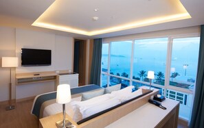 A hotel room with a bed, bedside table, lamp, TV, and a large window with a view of the sea. - Pattaya Sea View Hotel (Pattaya)