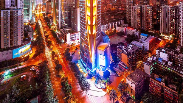 Un immeuble de grande hauteur doté d’une façade illuminée remarquable, entouré d’un environnement urbain dense, où se trouvent d’autres immeubles de grande hauteur.