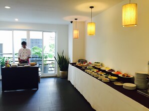 A buffet setup with a chef preparing food, a variety of dishes on a long table, and a view of the outdoors through a glass door.