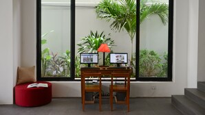 A workspace with two monitors, a red lamp, and a red ottoman with a book.