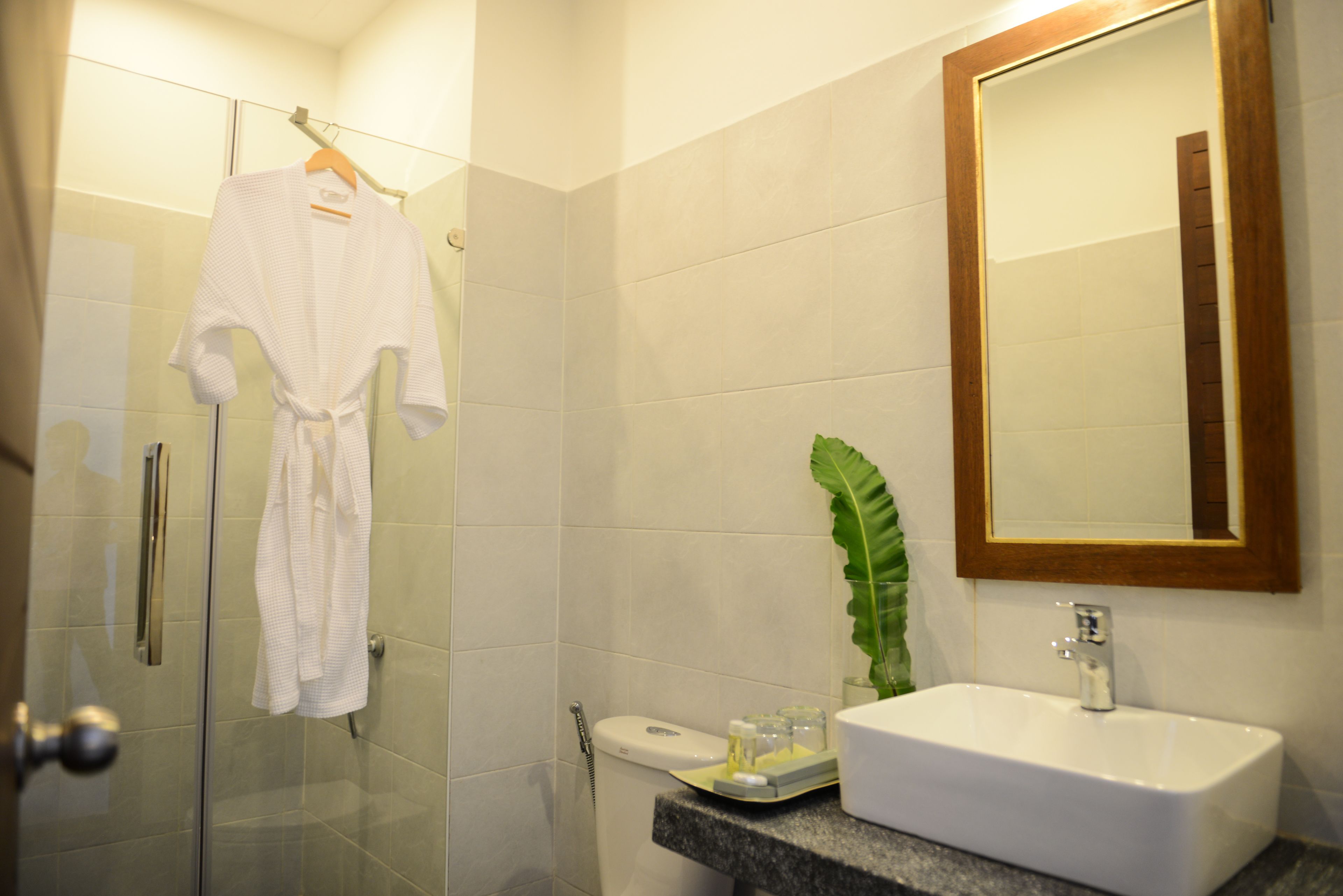 Un baño con cabina de ducha de vidrio, un lavamanos blanco y un espejo con marco de madera.