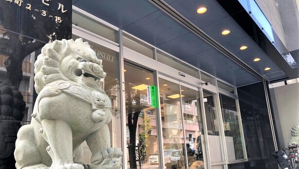 A building with a large stone lion statue in front, large glass windows, and a sign with Japanese characters. - Star Capsule Okinawa (Naha)