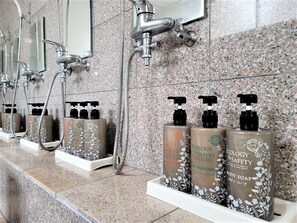A bathroom with multiple showerheads and a row of body soap dispensers on a marble countertop. - Star Capsule Okinawa (Naha)