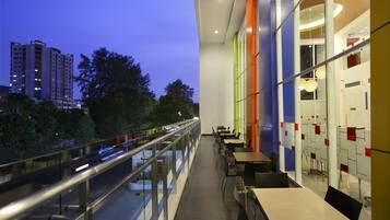 A modern restaurant with a glass railing overlooking a cityscape at dusk.