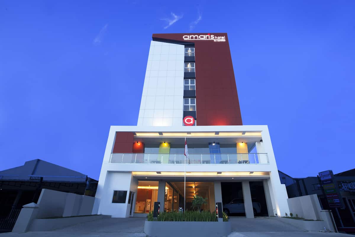 Un hôtel moderne, reconnaissable à son enseigne distinctive « Amans Hotel », à son entrée en verre et à son mât.