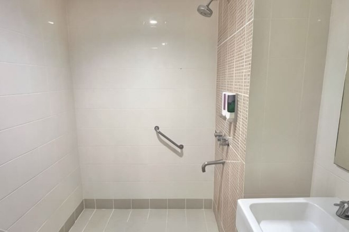 Un baño con azulejos blancos, ducha, lavamanos y dispensador de gel antibacterial.