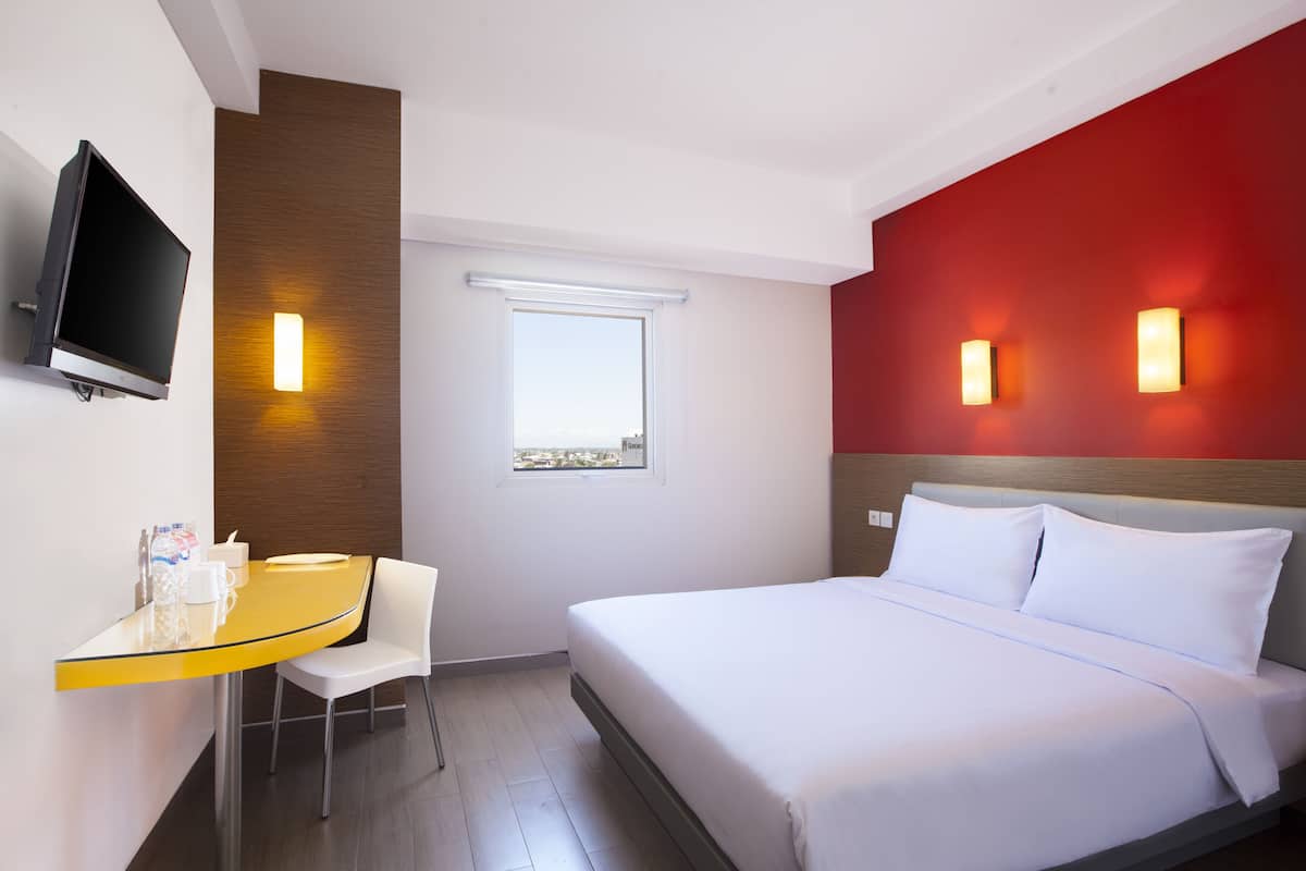 Une chambre d’hôtel comprenant un lit, un bureau avec une chaise, une télévision et deux lampes fixées au mur.