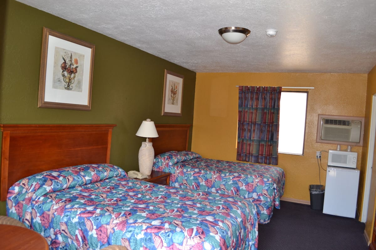Une chambre d’hôtel avec deux lits, une petite table avec une lampe, une poubelle et un four à micro-ondes.