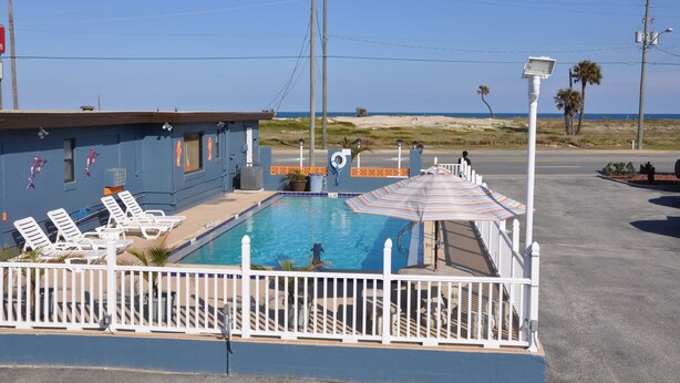 A pool area with lounge chairs, a lifeguard stand, and a view of the beach. - Atlantic Economy Inn (Daytona Beach)