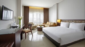 A hotel room with a large bed, a desk with a chair, a sofa, a coffee table, and a TV mounted on the wall. - Hotel Surya Yudha Purwokerto (Purwokerto)