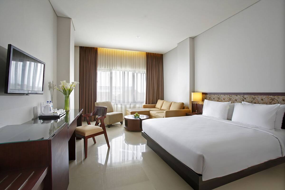 Une chambre d’hôtel avec un grand lit, un bureau avec une chaise, un canapé, une table basse et un téléviseur fixé au mur.