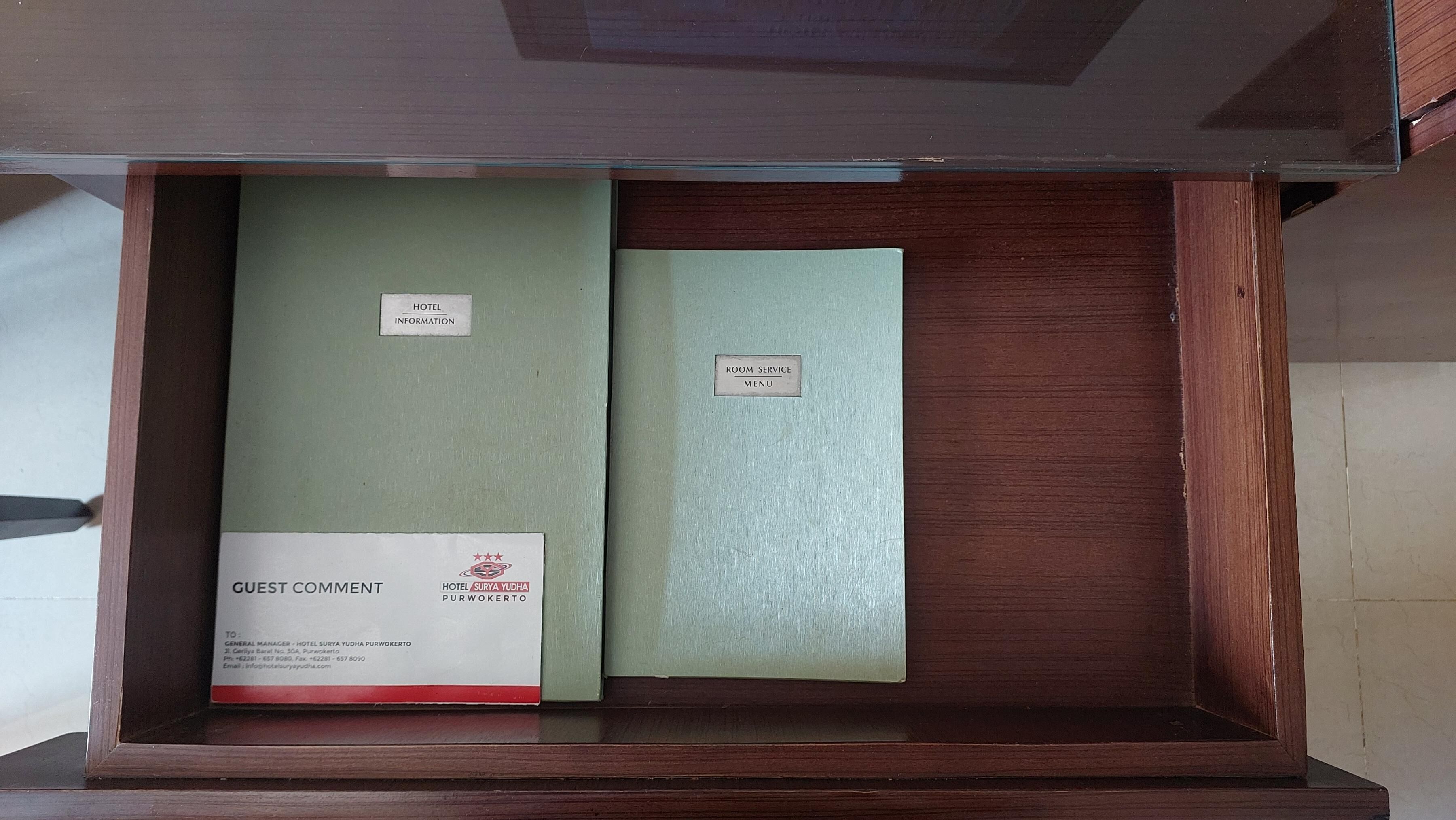 Un tiroir en bois contenant deux classeurs verts étiquetés « INFORMATIONS SUR L’HÔTEL » et « MENU DU SERVICE EN CHAMBRE ».
