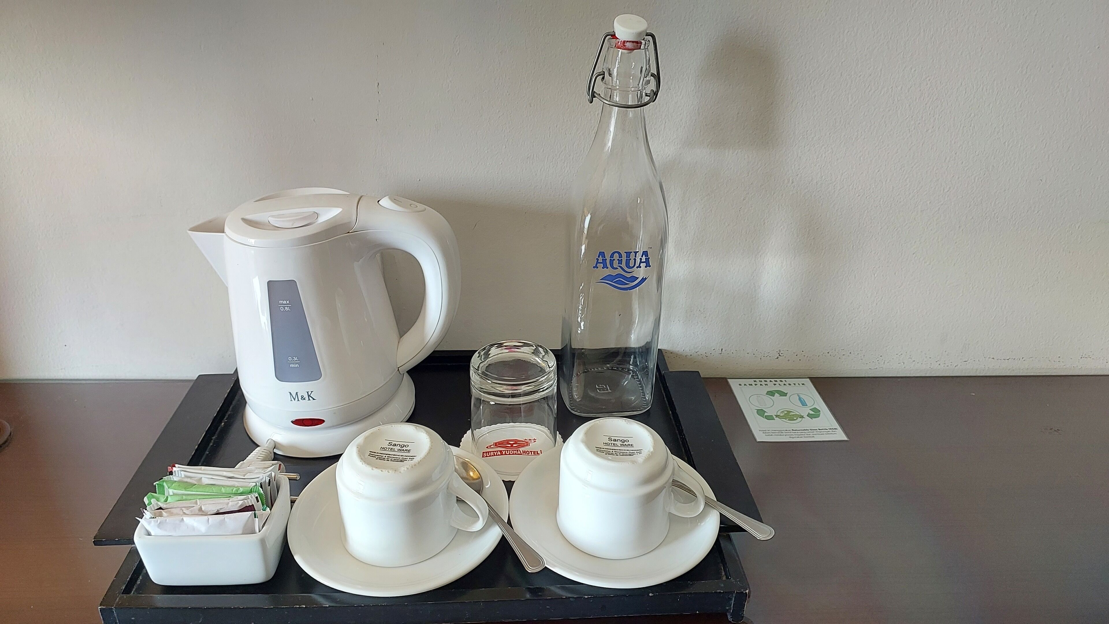 A tray with a white M&K kettle, a clear bottle labeled 'AQUA,' a glass jar, and white cups with lids and saucers.