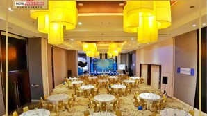 A hotel conference room with round tables, yellow chandeliers, and a large screen in the background. - Hotel Surya Yudha Purwokerto (Purwokerto)