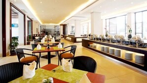 A modern dining area with tables and chairs, a buffet counter with plates, and a bright interior with natural light. - Hotel Surya Yudha Purwokerto (Purwokerto)