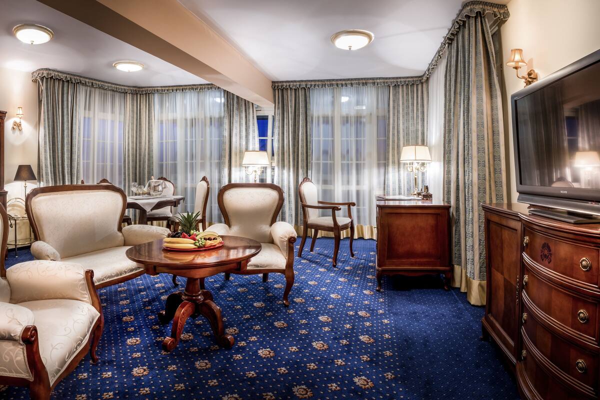 Ein Hotelzimmer mit einem großen Flachbildfernseher, einem Essbereich mit Tisch für zwei Personen und einer Sitzecke mit zwei Sesseln und einem Sofa.