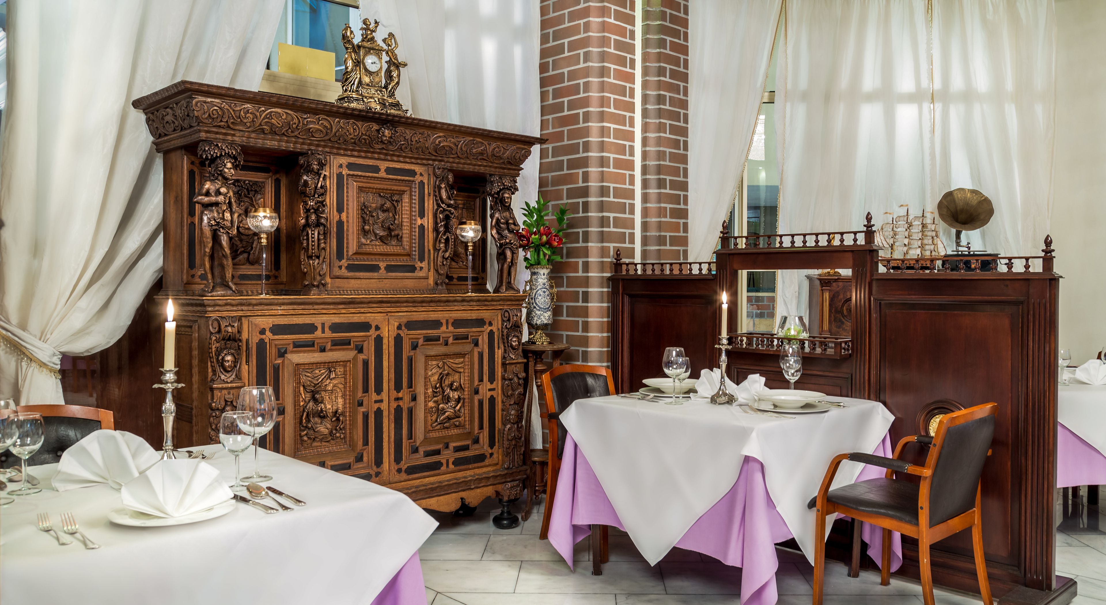 Un comedor con muebles de madera ornamentados, un pilar de ladrillo y un modelo de barco sobre un aparador.