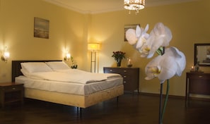 A hotel room with a bed, bedside lamps, a nightstand, a dresser, a mirror, and a vase with flowers. - Kobza Haus Old Town (Gdansk)
